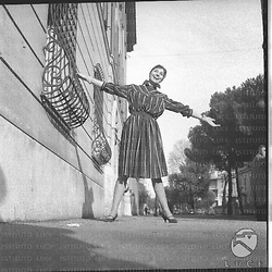Una modella con un vestito a strisce con le braccia aperte in una strada di Roma. Campo medio