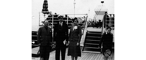Golfo di Napoli Foto di gruppo sul ponte della nave: un uomo in giacca, un ufficiale della marina ed una donna elegante con cappellino ed un fiore bianco all'occhiello della giacca; di lato si vede un bambino in divisa fascista