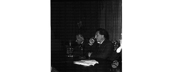 Carlo Levi seduto al tavolo degli oratori ripreso mentre beve un bicchiere d'acqua. Sulla sua destra è seduto Parri. Piano medio