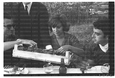 Carlo Lizzani, Anna Maria Ferrero e Gérard Blain al tavolo, durante una pausa delle riprese del film Il Gobbo, assaggiano qualcosa - piano americano
