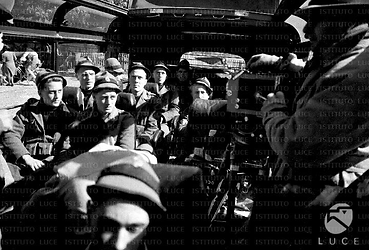 Il regista Arturo Gemmiti con la macchina da presa riprende gli alpini all'interno del furgone; piano americano