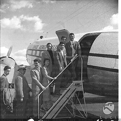 Membri di una squadra di calcio (?) e passeggeri posano sulla scaletta di un aereo della LAI in partenza. Campo lungo