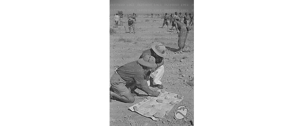 Due graduati in divisa coloniale controllano una carta mentre i soldati lavorano il terreno circostante con delle vanghe