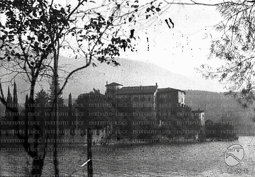 Veduta di una residenza ottocentesca (?) con torre cicolare e mura merlate sita su una penisoletta in mezzo al verde di un bacino lacustre o di una laguna. Campo lungo