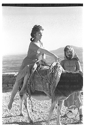 Gina Lollobrigida in sella ad un mulo vicino al mare e vicino una bambina sul set del film 'Pane amore e gelosia' - totale