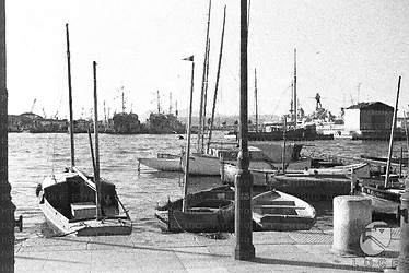 Un tratto del porto di Tolone: barche da pesca attraccate vicino al molo, navi da guerra francesi semi-affondate sullo sfondo