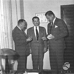 Tre uomini in piedi in un ufficio sorridono, forse ad uno dei tre viene conferita un'onorificenza; piano americano