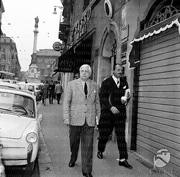 Giorgio De Chirico passeggia in una via nei pressi di Piazza di Spagna in compagnia di un uomo; campo medio