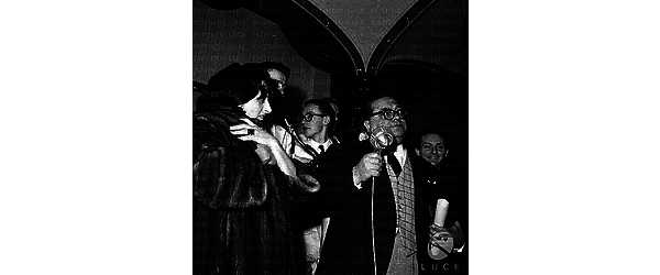 Aldo Fabrizi sul palco parla ad un microfono e tiene in mano una pergamena; accanto a lui Anna Magnani