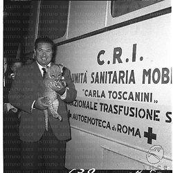 Angelo Lombardi, tenendo in braccio un leoncino, posa accanto ad un'unità sanitaria mobile della C.R.I. per le trasfusioni. Piano americano