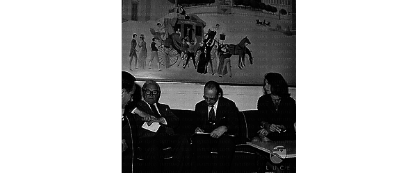 Claude Rains seduto su su un divano con dei giornalisti e Maya Brent