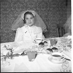 Bambina con abito della comunione seduta ad un tavolo - piano medio