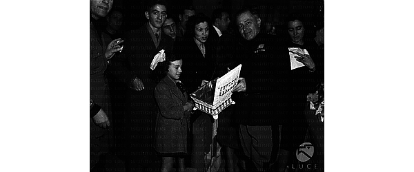 Roma Bevione consegna una scatoletta a una bambina durante la Befana Fascista dell'INA