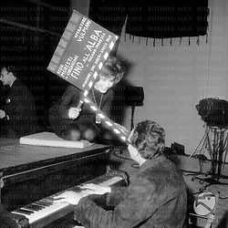 Gabriella Farinon seduta sopra il pianoforte con in mano il ciak del film; Vulpiani suona