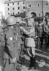 Roma Mussolini passa in rassegna i Battaglioni "M" schierati in piazza Bocca della Verità a Roma in occasione del primo annuale della loro fondazione ed appunta una decorazione sul petto di un legionario