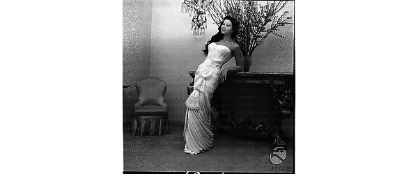 Interno. Laya Raki posa in una stanza, in elegante abito da sera bianco lungo, appoggiata a una consolle barocca. Totale