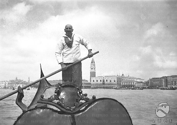 Venezia Gondoliere in piedi con remo in mano conduce una gondola nel bacino antistante la laguna. Campeggia sullo sfondo il campanile di San Marco
