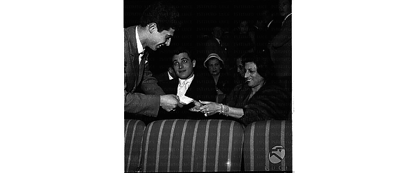 Anna Magnani, con Gabriele Tinti, mentre un giovane le porge un foglio, seduta nella sala del concerto di Hampton - piano americano