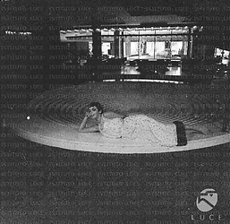 Barbara Steele, a piedi nudi, distesa su una struttura circolare all'interno dell'Hotel Hilton; campo medio