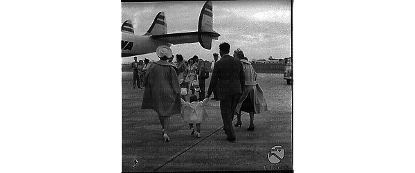 Gina Lollobrigida ripresa di spalle in aereoporto mentre si avvia verso l'aero, con fglio e marito per mano - totale