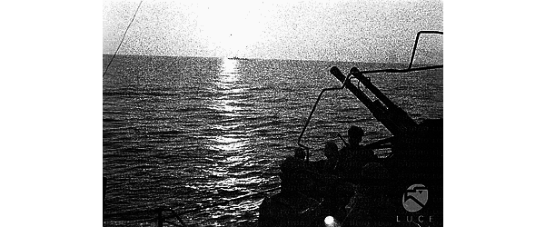 Marinai in assetto da guerra vicino ad una batteria anti-aerea, un'altra unità della squadra italiana sullo sfondo