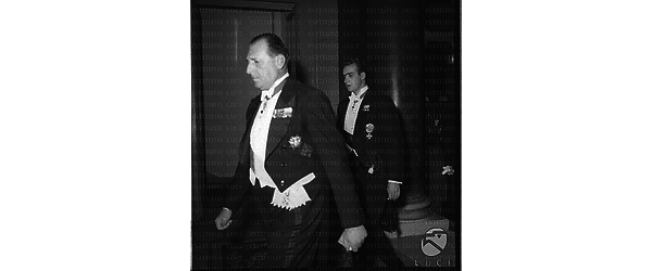 Don Juan  di Borbone conte di Barcellona ripreso elegantemente vestito mentre cammina con passo rapido seguito dal figlio Juan Carlos forse all'interno del Grand Hotel - totale
