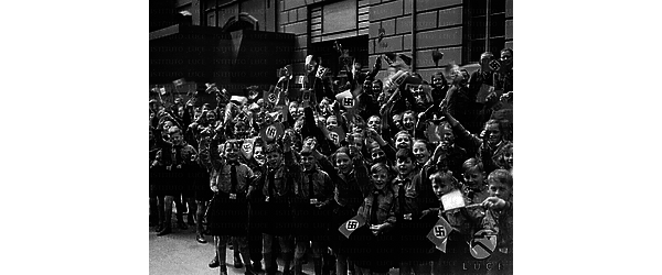 Berlino Folla di bambini della Gioventù hitleriana, radunata sul marciapiede di una strada berlinese, sventola bandierine italiane e con la croce uncinata
