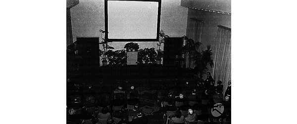 Roma Pubblico di spettatori attende, in una sala - con grande schermo - della sede dell'O.N.M.I., la proiezione di documentari Luce sull'attività dell'ente