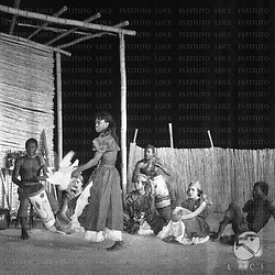 Campo medio, danzatrice balla con una colomba in mano, percussionisti e danzatrici accompagnano la danza
