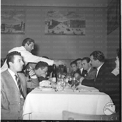 Scorcio di un tavolo in un ristorante, dove sono seduti dipendenti della Ferrania, intenti a mangiare, mentre un cameriere li serve. Campo medio