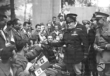 Bologna Benito Mussolini è ritratto mentre fa una carezza, guardando altrove e sorridendo, sulla guancia di un mutilato, seduto con le grucce insieme ad altri feriti di guerra, nel giardino del centro ortopedico "Putti"
