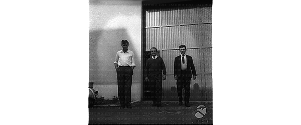 Tre uomini ripresi in un esterno, davanti ad un edificio, forse uno dei capannoni dove è in parte ospitato il laboratorio di fisica Frascati - campo medio