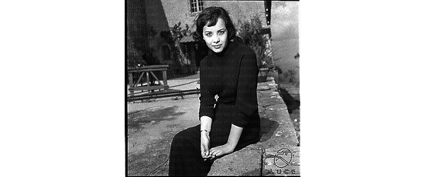 La Balducci in posa mentre è seduta su un muretto di un cortile. Piano americano