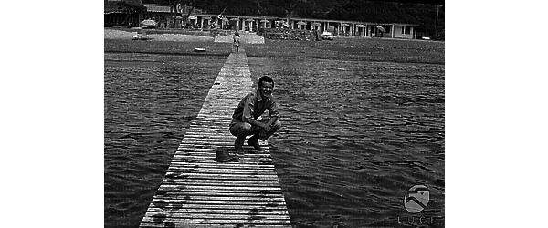 Serge Reggiani accovacciato su un molo a passerella