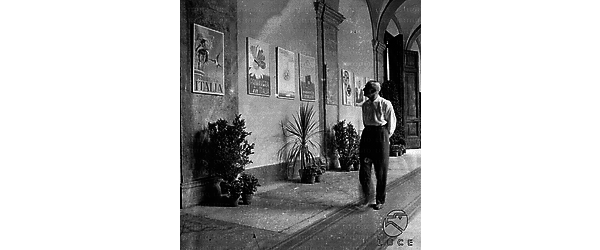 Visitatore passa sotto il portico del cortile del palazzo della Sapienza dove sono esposti manifesti di propaganda turistica intitolati alla "Primavera in Italia" - campo medio