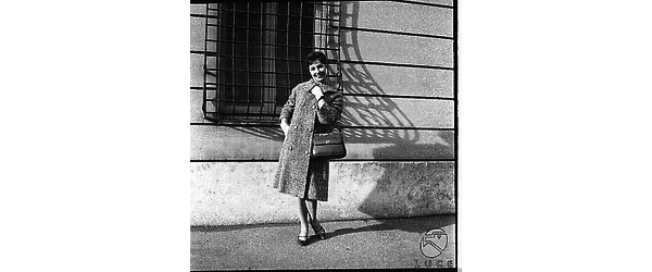 Una modella con un cappotto su un marciapiede di una strada di Roma. Campo medio