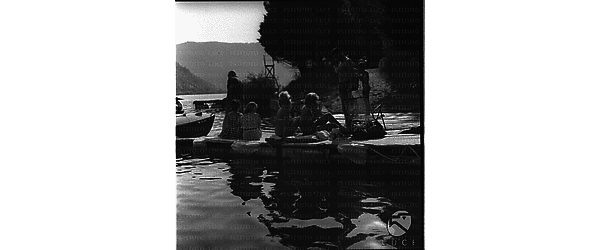 Brigitte Bardot e una donna (Berojer ?) in costume sedute su un materassino in compagnia di un uomo su un piccolo molo del lago di Piediluco - campo medio