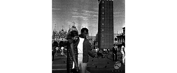Michel Roney con una donna a piazza San Marco e sulla mano una colomba. Piano americano