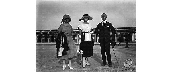 Due donne  in abito da passeggio in posa accanto ad  un elegante signore