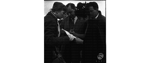 Vera Tschechowa ripresa accanto ad altre persone mentre firma qualcosa - piano americano