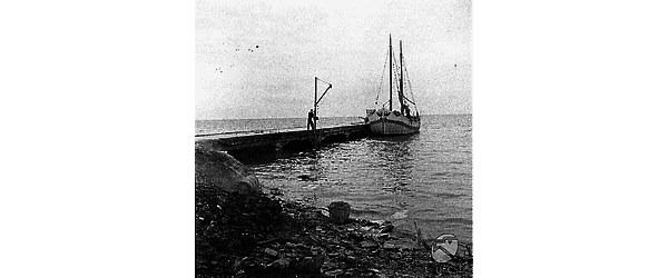 Izola Barca da pesca ancorata accanto ad un molo; in primo piano è inquadrata una parte di battigia, coperta di scatolette di latta ed altri materiali di scarto