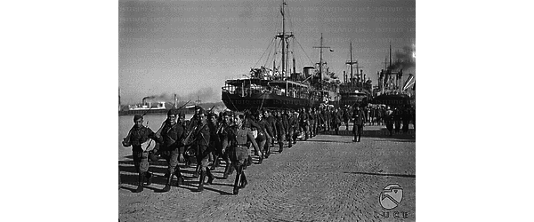Una colonna di soldati italiani si allontana marciando dal molo dove si trovano le navi con cui sono giunti a Durazzo
