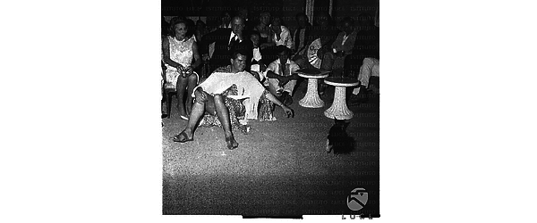 Roloff Beny, in costume di tipo africano, seduto a terra nella terrazza di casa sua con i suoi ospiti - totale