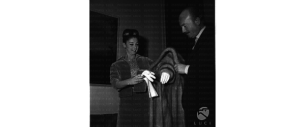 Anna Maria Pierangeli in abito elegante mentre viene aiutata da Armando Trovajoli a sfilarsi la pelliccia - piano americano