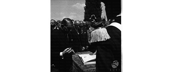Coty, ripreso durante la visita al cimitero militare francese a Monte Mario, attende con una penna in mano per apporre la firma su un registro. Alle sue spalle gruppo di autorità tra cui Pineau e un generale francese. Piano medio