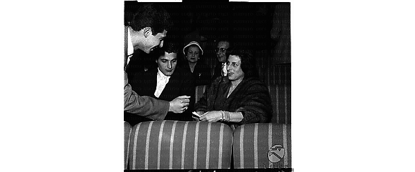 Anna Magnani, ripresa con Gabriele Tinti, mentre un altro le parla, seduta nella sala del concerto di Hampton - piano medio