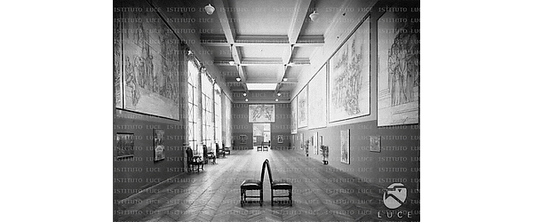 Lunga sala del palazzo delle Esposizioni ripresa in prospettiva centrale. Alle pareti sono allestiti grandi cartoni di De Carolis -  Campo lungo
