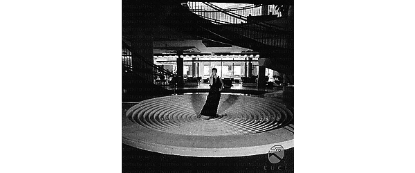 Barbara Steele in piedi su una struttura circolare a cerchi concentrici all'interno dell'Hotel Hilton; campo lungo