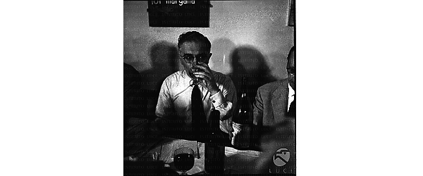 Lo scrittore Giancarlo Vigorelli beve un bicchiere di vino seduto al tavolo del ristorante 'da Angelino'. Piano medio
