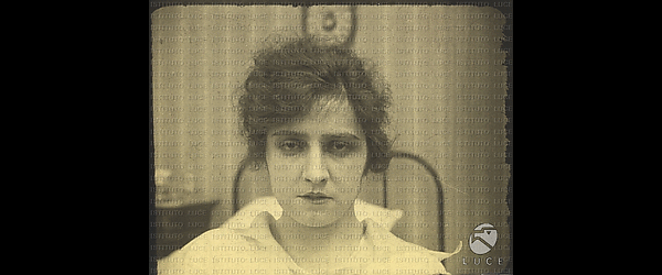 L'attrice Maria Jacobini in una scena del film "Come le foglie", appare seduta su un letto, di cui si intravede la spalliera. Ha un'espressione triste e i capelli disordinatamente raccolti.